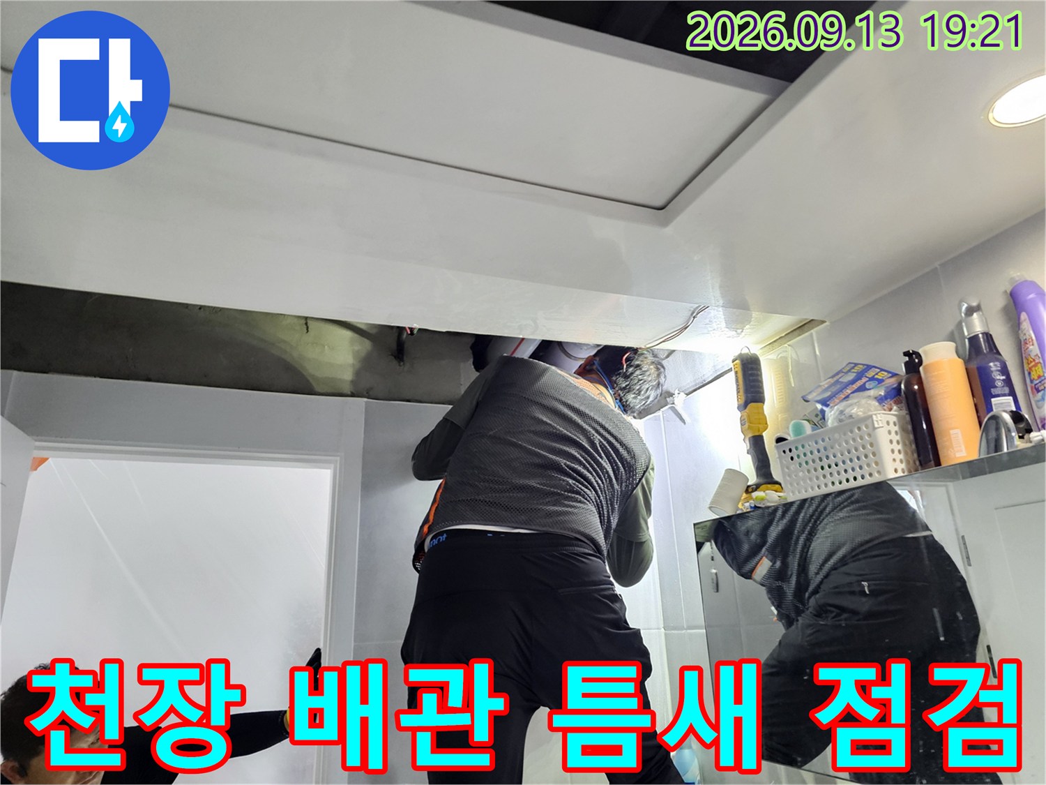 어두운 천장 내부의-배관 연결 부위를 조명으로 세밀하게 조사하는 모습입니다.