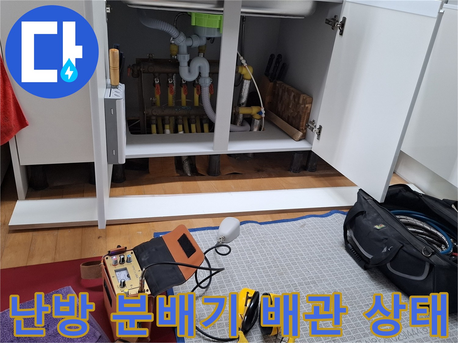싱크대 하부장 내부에 노출된 난방 분배기와 각종 배관 연결 부위