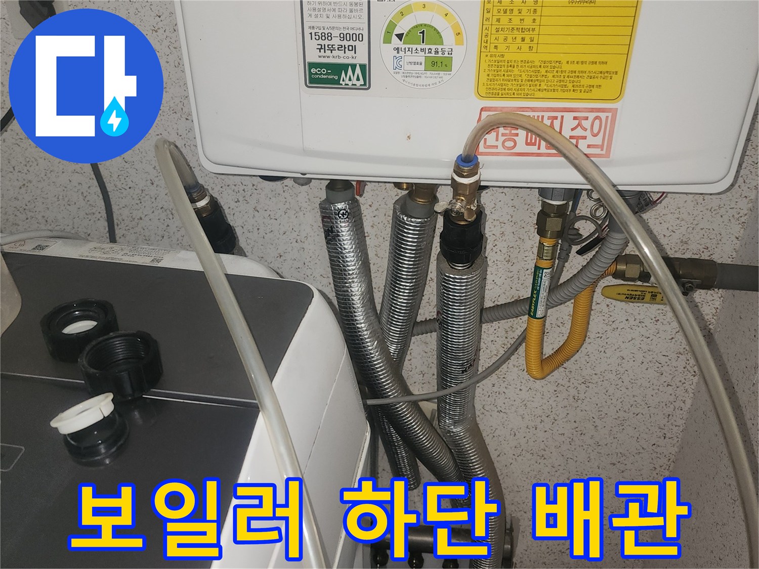 보일러 본체 아래로 뻗어 나온 은색 자재와 노란색 유연한 관