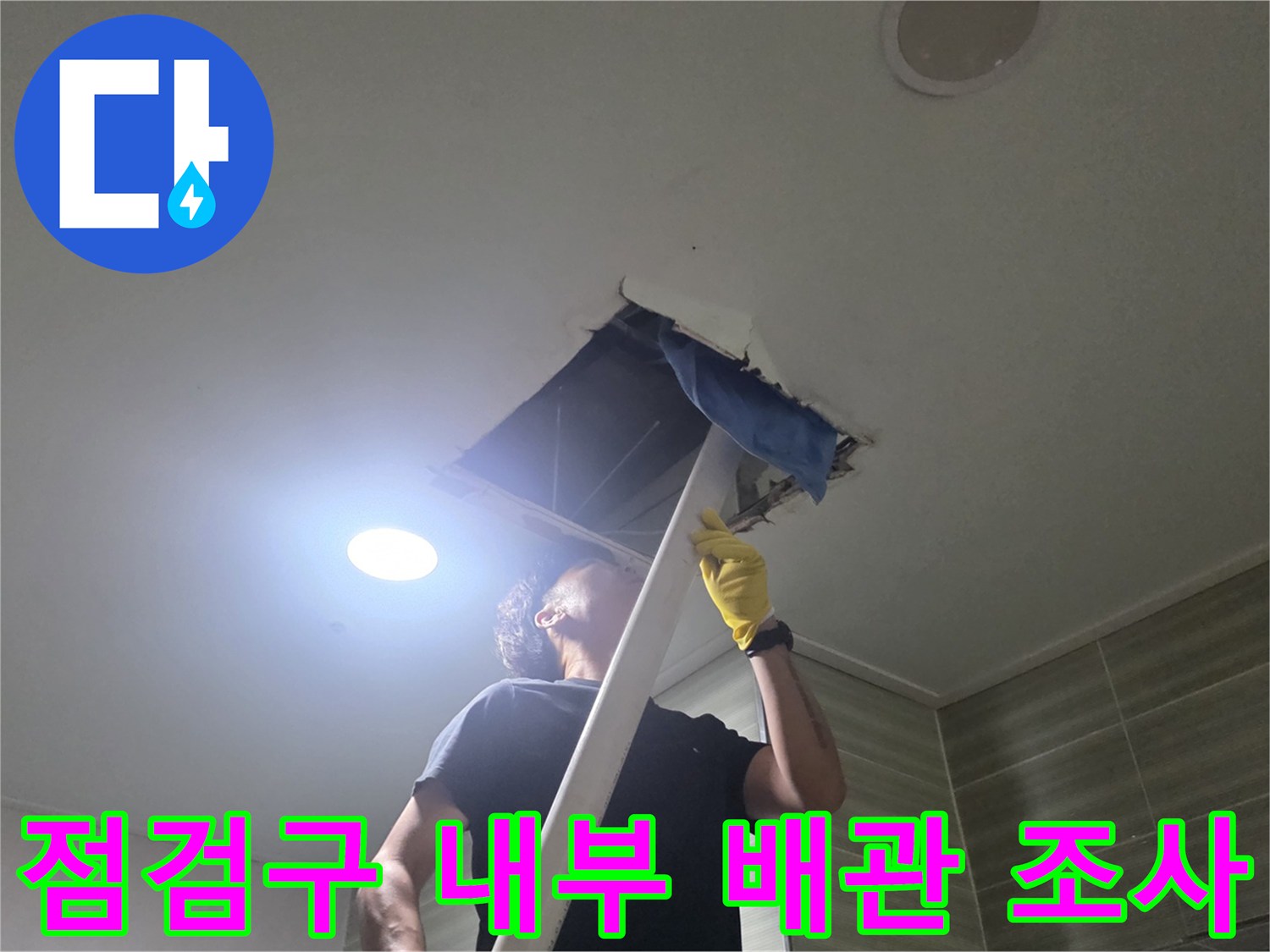 천장 점검구를 열고 조명을 사용하여 배관 상태를 확인하는 모습